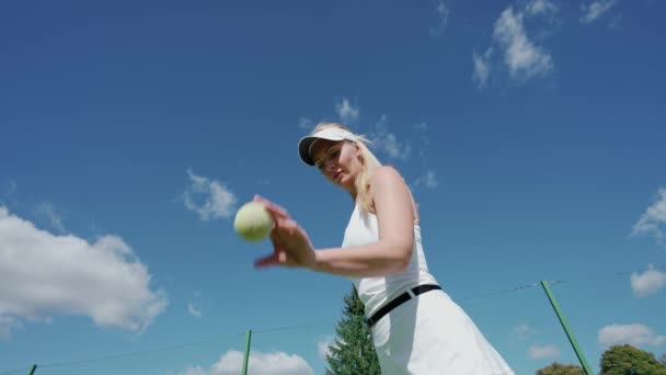 Ung kvinna tennisspelare träffar en boll från golvet i en utomhus domstol, låg vinkel vy, träningsdag. — Stockvideo