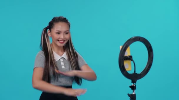꽤 나 아시아인 여성들이 푸른 배경의 음악에 맞춰 춤을 추고 소셜 네트워크를 위해 스마트폰으로 자신의 비디오를 찍습니다.. — 비디오