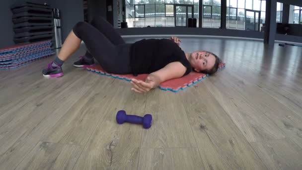 Надмірна вага жінки, що лежить на килимі у фітнес-клубі, дуже втомлена, що викидає гантелі і не може дихати — стокове відео