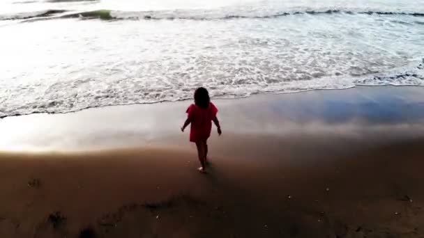 Γυναίκα με κόκκινο φόρεμα περπατώντας στο νερό από την παραλία άμμο στην παραλία κατά το ηλιοβασίλεμα, εμπνέει — Αρχείο Βίντεο