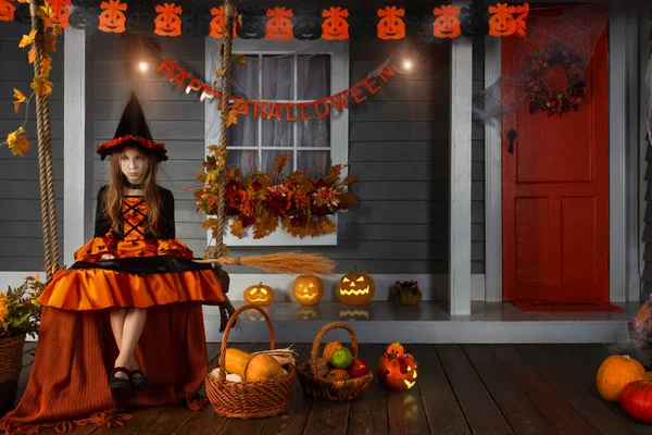 穿着黑帽女巫服装 头戴橙色南瓜篮 脸上带着恐怖的糖果和糖果 坐在秋千上 准备庆祝秋节假期 — 图库照片
