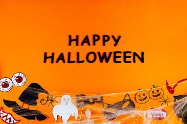 Örümcekağıyla kutlama için sahne donanımları, maskeler ve dekorlar tuvalin dibine saçılmıştır. Turuncu arka planda parti aksesuarları. Tebrik kartı şablonu. Siyah yazıt Mutlu Cadılar Bayramı.