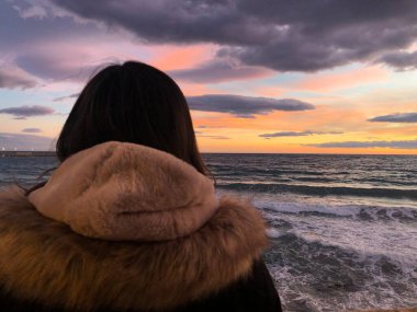 Arkadan gelen yürüyüşçü kadın denizin üzerinden güneşin doğuşuna bakıyor.