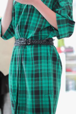 Siyah kuşaklı yeşil bir ekose gömlek. Modelin ayakta duruşu.