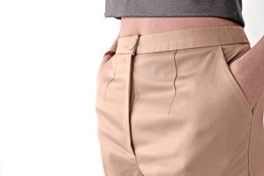 Bej pantolonlu bir kadın heykeli kendine güvenerek yan duruyor, ellerini pantolonunun cebinde tutuyor. Vücudun bir kısmı görünür. Konsept: İş kadını, bireysel terzilik, giyim markası.