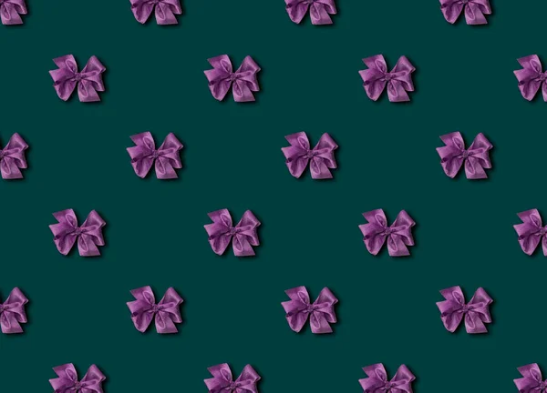 Arco púrpura para decorar regalos sobre un fondo verde. Bonito lazo atado. Foto de un paquete de regalo con un patrón sin costuras. —  Fotos de Stock