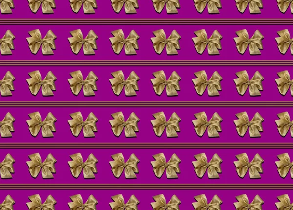 Guld bågar för att dekorera gåvor på en lila bakgrund. Vackert bunden rosett, ränder mellan bågarna. Foto av ett gåvopaket med ett sömlöst mönster. — Stockfoto