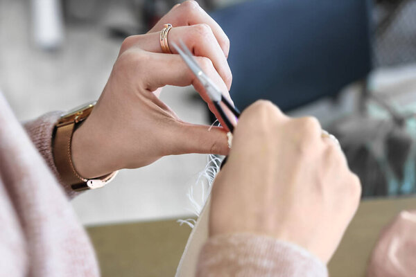 Female hands, white, 30-35 years old, cuts the seam with small scissors. Clothes repair in the studio, remodels. Concept: atelier, sewing courses, sewing hobbies.