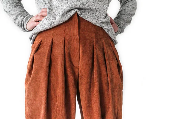 Önünde beyaz bir kadın duruyor, kazak ve terracotta pantolon giymiş.. 