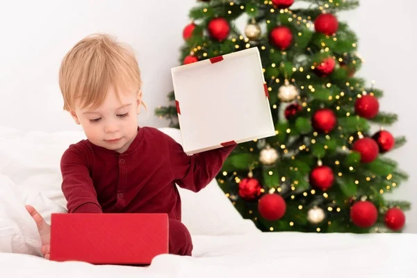 Sarışın, beyaz bir bebek yatak odasında Noel ağacının yanında kırmızı hediye kutusunu alır. Kış tatilini evde geçirir. Bebek, çocuk, pijamalı bebek için yeni yıl hediyesi verir..