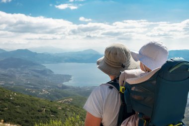Baba sırt çantasında bebek taşıyor, güzel bir göl, dağ gibi görünüyor. Aile doğada güzel bir yerde yürüyüş yapıyor. Bebek, çocuk konseptiyle tatiller, açık hava aktiviteleri, aktif iyileşme kavramı..