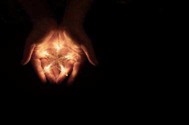Avuçlarda parlayan bir yıldız, siyah bir arka planda. Beş köşeli parlak bir yıldız ellerinde, yeni yıl ve Noel yaklaşıyor. Noel ve Yeni Yıl arifesinde süslemeler ve çelenkler..