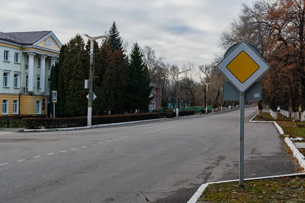 道路标志 在城市的道路上 在主干道上的一个标志 后面有一座公共建筑 白色锯齿状 在路柱上 — 图库照片