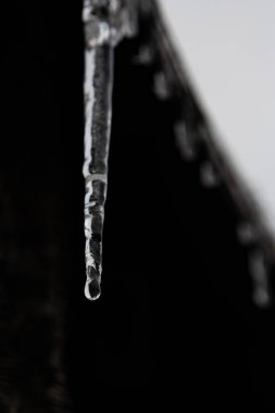 Donmuş bir buz saçağı çatıdan sarkıyor, siyah bir zeminde. Kışın çatıda bir buz saçağı asılı, soğukta su donmuş..