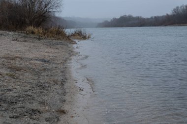 Kıyı şeridi, suyun ve nehrin karasının buluşması. Küçük dalgaların kıyıya vurduğu bir nehir. Sabahın erken saatlerinde, nehir yatağında sis bulutu vardı..