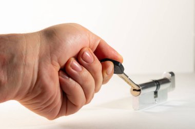Anahtarı parmaklarında olan bir el, anahtar deliğinin yanında, arka planda. Avuç içinin içinde düz bir anahtar, kilitten bir larva, hafif bir arka plan..