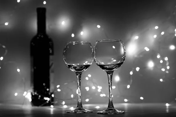 İki boş şarap kadehi ve bir şişe şarap, siyah beyaz. Şarap bardakları ve bir şişe şarap, ışıklardan gelen bir bokeh.