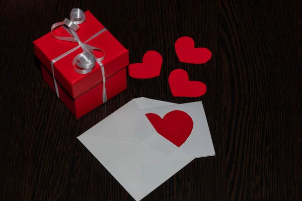 A gift box and a Valentine's Day greeting card. Attributes of Valentine's day, on a brown, textured background, with a wood texture.
