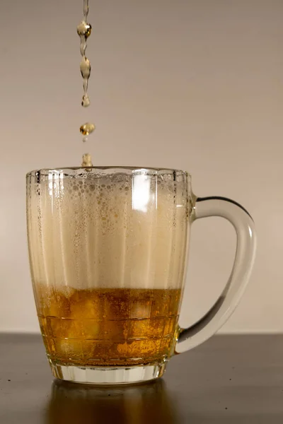 stock image The glass is filled with beer and foam, beer pours into the glass. Transparent glass with light beer and thick foam.