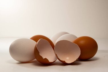 Birkaç kahverengi ve beyaz yumurta bir arada istiflenir ve ön planda kırık bir kahverengi yumurta vardır. Kahverengi ve beyaz tavuk yumurtaları, arka planda, Paskalya arifesinde..