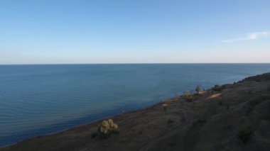 Gün batımında deniz ve yüksek sahil. Ağaçlar ve toprak yol. Drone görünümü.