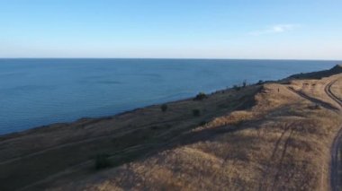 Gün batımında deniz ve yüksek sahil. Ağaçlar ve toprak yol. Drone görünümü.