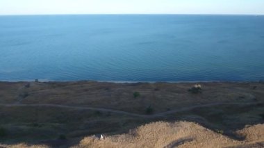 Gün batımında deniz ve yüksek sahil. Ağaçlar ve toprak yol. Drone görünümü.