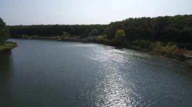 Nehir suyunun yüzeyinde güneş parlıyor. Gölün kıyısındaki ağaçlar. Drone görünümü