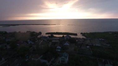 Belosaraiskaya Tükürüğü 'ndeki sahil köyünün üzerindeki bulutlarda gün batımının insansız hava aracı görüntüsü.