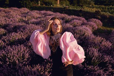 Güzel bir kadın lavanta tarlasında gün batımında siyah ve pembe elbiseler içinde dinleniyor. Çiçek tarlasındaki sarışın kadın. Provence.