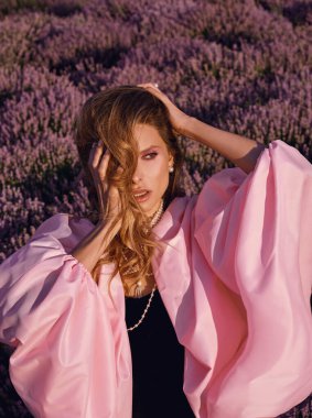 Güzel bir kadın lavanta tarlasında gün batımında siyah ve pembe elbiseler içinde dinleniyor. Çiçek tarlasındaki sarışın kadın. Provence.