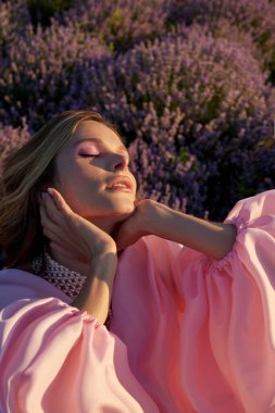 Güzel bir kadın lavanta tarlasında gün batımında siyah ve pembe elbiseler içinde dinleniyor. Çiçek tarlasındaki sarışın kadın. Provence.