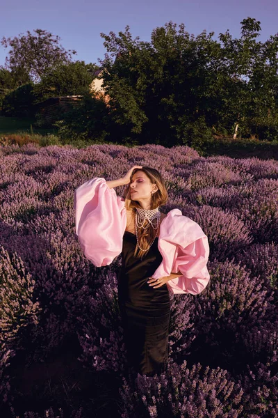 Güzel bir kadın lavanta tarlasında gün batımında siyah ve pembe elbiseler içinde dinleniyor. Çiçek tarlasındaki sarışın kadın. Provence.