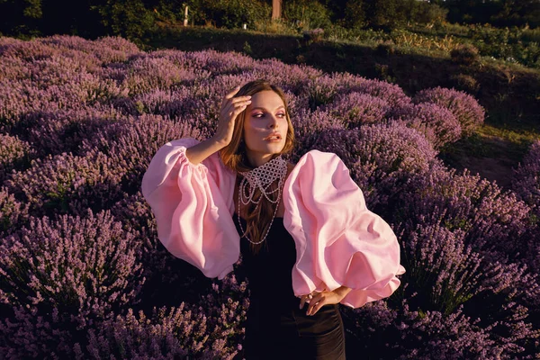 Güzel bir kadın lavanta tarlasında gün batımında siyah ve pembe elbiseler içinde dinleniyor. Çiçek tarlasındaki sarışın kadın. Provence.