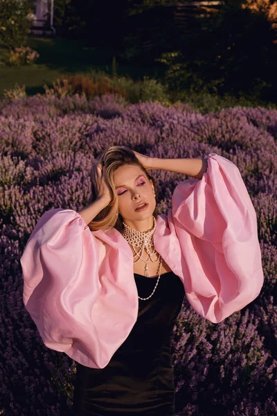 Güzel bir kadın lavanta tarlasında gün batımında siyah ve pembe elbiseler içinde dinleniyor. Çiçek tarlasındaki sarışın kadın. Provence.