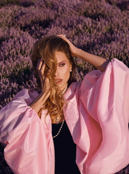 Güzel bir kadın lavanta tarlasında gün batımında siyah ve pembe elbiseler içinde dinleniyor. Çiçek tarlasındaki sarışın kadın. Provence.
