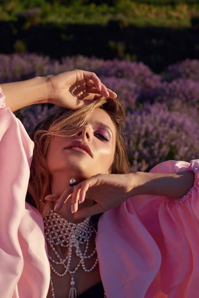 Güzel bir kadın lavanta tarlasında gün batımında siyah ve pembe elbiseler içinde dinleniyor. Çiçek tarlasındaki sarışın kadın. Provence.