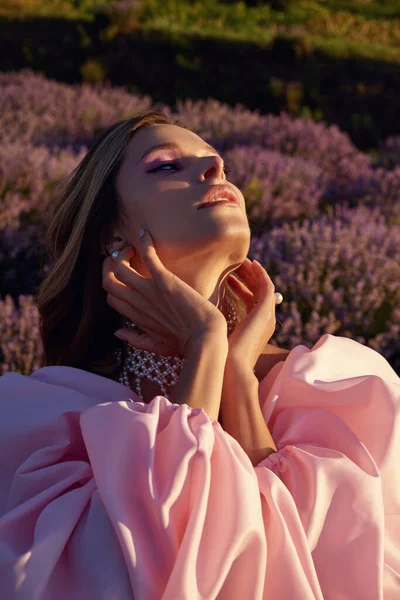 Güzel bir kadın lavanta tarlasında gün batımında siyah ve pembe elbiseler içinde dinleniyor. Çiçek tarlasındaki sarışın kadın. Provence.