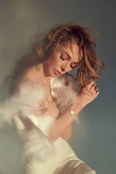 Genç ve çekici kadın modeller mücevherlerinizi sunuyor. Tüylü beyaz elbiseler giyin. Çıplak makyaj, mükemmel cilt, uzun saç. Beyaz arkaplan.