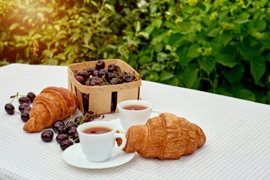 Beyaz arka planda taze kruvasan ve kirazlı siyah çay. Bahar kahvaltısı kavramsal kompozisyonu