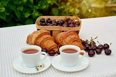 Beyaz arka planda taze kruvasan ve kirazlı siyah çay. Bahar kahvaltısı kavramsal kompozisyonu
