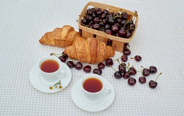 Beyaz arka planda taze kruvasan ve kirazlı siyah çay. Bahar kahvaltısı kavramsal kompozisyonu