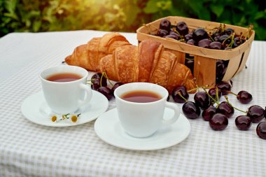 Beyaz arka planda taze kruvasan ve kirazlı siyah çay. Bahar kahvaltısı kavramsal kompozisyonu