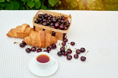 Beyaz arka planda taze kruvasan ve kirazlı siyah çay. Bahar kahvaltısı kavramsal kompozisyonu
