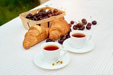 Beyaz arka planda taze kruvasan ve kirazlı siyah çay. Bahar kahvaltısı kavramsal kompozisyonu