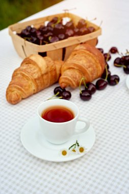 Beyaz arka planda taze kruvasan ve kirazlı siyah çay. Bahar kahvaltısı kavramsal kompozisyonu