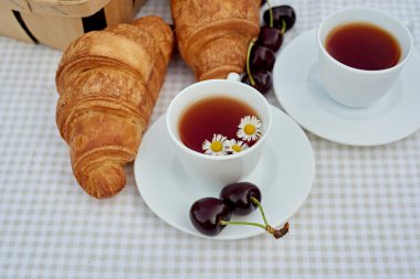 Beyaz arka planda taze kruvasan ve kirazlı siyah çay. Bahar kahvaltısı kavramsal kompozisyonu