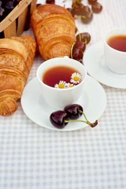 Beyaz arka planda taze kruvasan ve kirazlı siyah çay. Bahar kahvaltısı kavramsal kompozisyonu