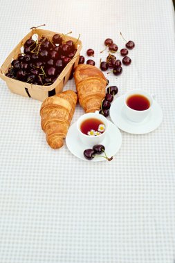 Beyaz arka planda taze kruvasan ve kirazlı siyah çay. Bahar kahvaltısı kavramsal kompozisyonu