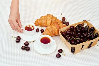 Beyaz arka planda taze kruvasan ve kirazlı siyah çay. Bahar kahvaltısı kavramsal kompozisyonu